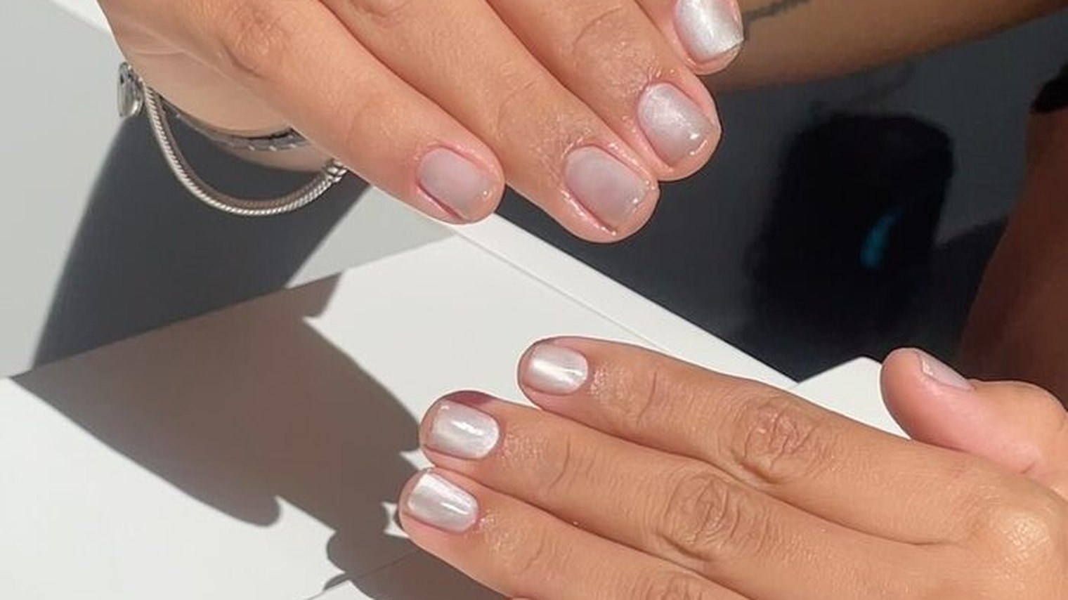 Unhas curtas com acabamento perolado refletindo a luz natural — trabalho de Priscila Dias
